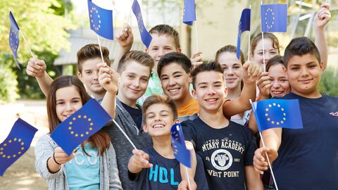 Schülerinnen und Schüler schwenken kleine EU-Fahnen.