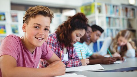 Schülerinnen und Schüler sitzen in Schulbibliothek und lernen. 