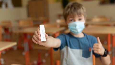 Schüler mit Maske hält einen negativen Antigentest hoch. 