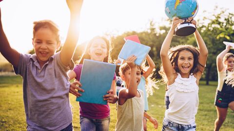 Kinder mit Schulbüchern und Globus laufen über die Wiese.
