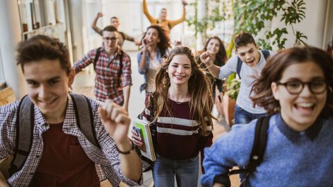 Schülerinnen und Schüler laufen fröhlich durch den Schulflur. 