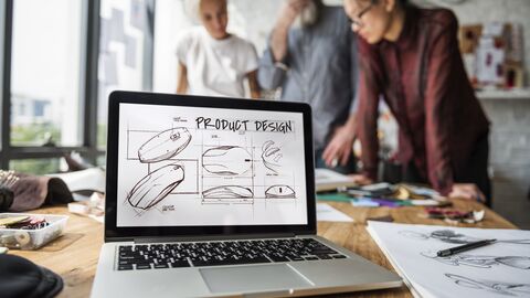 Laptop mit der Aufschrift Produktdesign steht geöffnet in einer Agentur.