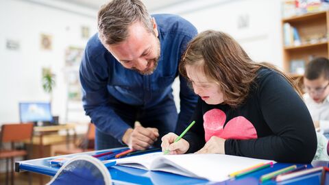 Lehrer unterstützt eine Schülerin bei den Aufgaben.
