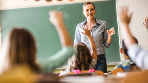 Lehrerin unterrichtet eine Klasse und Schülerinnen und Schüler melden sich.