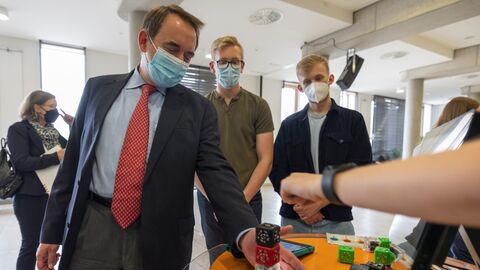 Kultusminister Lorz steht an einem Tisch, hält die Hände neben einen Würfelblock.