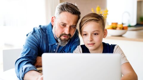 Vater zeigt seinem Sohn etwas am Laptop.