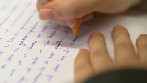 Eine Jugendliche schreibt einen Brief mit der Hand. 