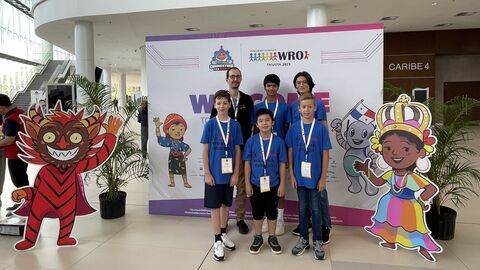 Fünf Schüler und eine Betreuungsperson stehen vor einem Aufsteller der World Robot Olympiad in Panama City.