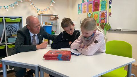 Kultusminister Schwarz sitzt gemeinsam mit Schüler und Schülerin an Tisch und schaut in ein Buch