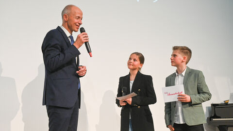 Kultusminister auf Bühne im Gespräch mit Schülerin und Schüler