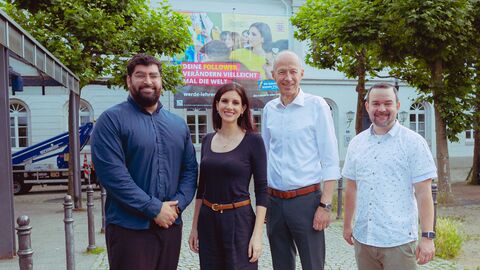 Kultusminister Schwarz gemeinsam mit drei weiteren Personen. Im Hintergrund hängt an einer Wand ein Plakat der Initiative „Die Zukunft braucht Dich! Als Lehrerin oder Lehrer“.