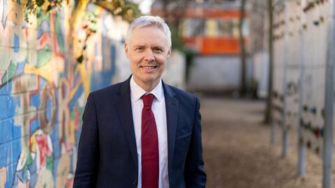 Portraitfoto von Dr. Manuel Lösel vor einer bunten Wand in einem Schulhof.