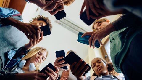 Jugendliche stehen in einem Kreis und schauen auf ihr Handy