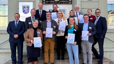 Mehrere Personen stehen auf Treppe und lachen in Kamera. Einige halten Zertifikate in den Händen