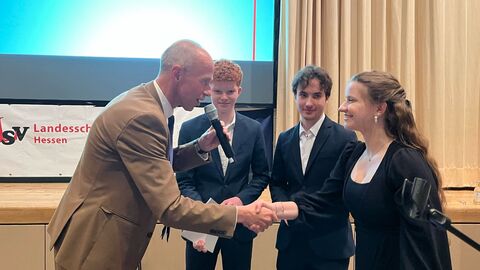 Kultusminister Armin Schwarz schüttelt einer Schülerin der Landesschülervertretung die Hand. Zwei weitere Schüler stehen im Hintergrund und lächeln freundlich.