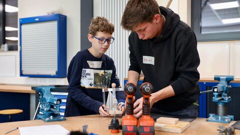 Gemeinsames Werken: Ein älterer Schüler zeigt einem Grundschüler, wie man an der Werkbank ein Holzprojekt bearbeitet.