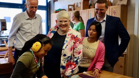 Zwei Schülerinnen arbeiten konzentriert an der Werkbank. Minister Armin Schwarz zeigt großes Interesse an der praktischen Arbeit.