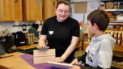 Eine Berufsschülerin erklärt einem Grundschüler den Umgang mit Schleifklotz und Holzplatte.
