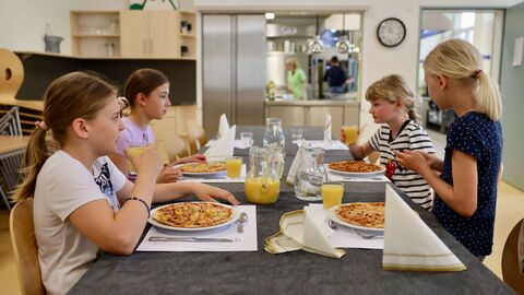 Gemeinsames Essen nach getaner Arbeit: Vier Grundschülerinnen sitzen an einem gedeckten Tisch und genießen ihre selbstgemachte Pizza.