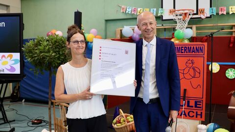 Bildungsminister Schwarz steht mit der Schulleiterin zusammen und hat ein Zertifikat überreicht.