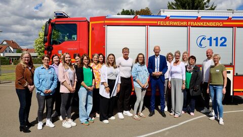 Kultusminister Armin Schwarz steht gemeinsam mit Lehrerinnen und Lehrern vor einem roten Löschgruppenfahrzeug der Feuerwehr Frankenberg auf dem Schulhof.