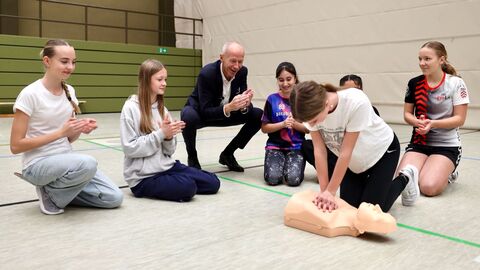 Mehrere Schülerinnen knien in Turnhalle. Eine Schülerin übt an Puppe Wiederbelebung.