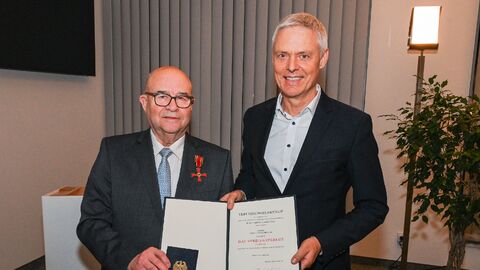 Zwei Männer stehen nebeneinander und halten eine Urkunde hoch.