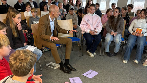 Minister Schwarz sitzt mit Schülern in einem Stuhlkreis. Auf dem Boden liegen Zettel mit Wörtern wie "Respekt" und "Meinungsfreiheit"