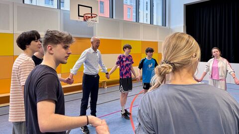 Minister Schwarz und Schüler und Schülerinnen stehen in einer Turnhalle im Kreis und halten sich an den Händen