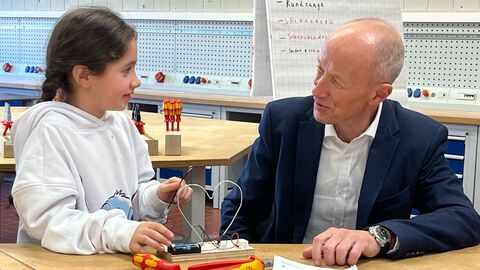 Bildungsminister Schwarz sitzt am Tisch mit einem Mädchen, die gerade etwas am bauen ist.