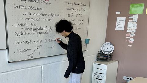 Ein Jugendlicher steht an einem Whiteboard und schreibt etwas darauf.